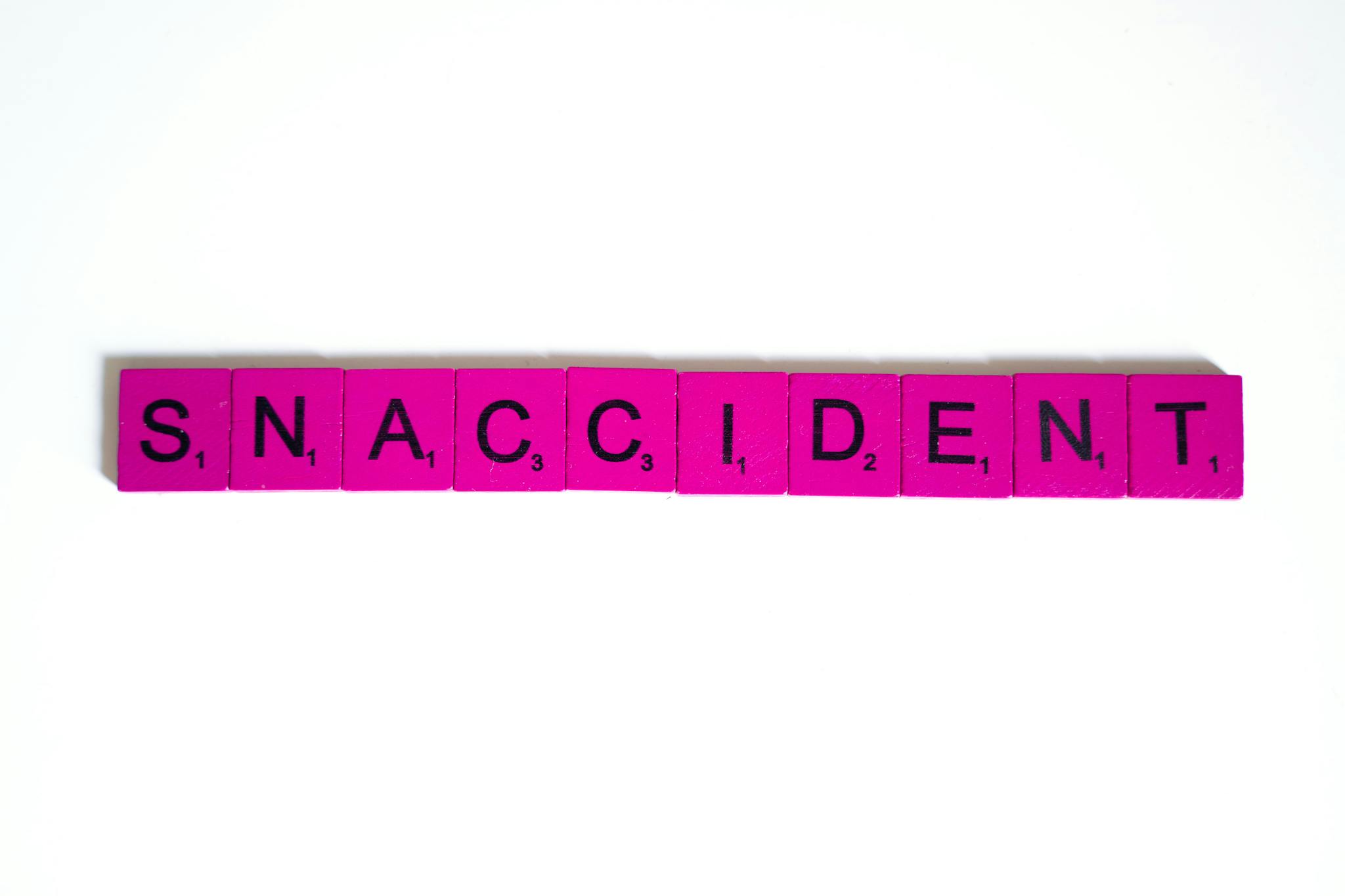 Pink letter tiles arranged on a white background spelling 'Snaccident' in a playful flat lay.